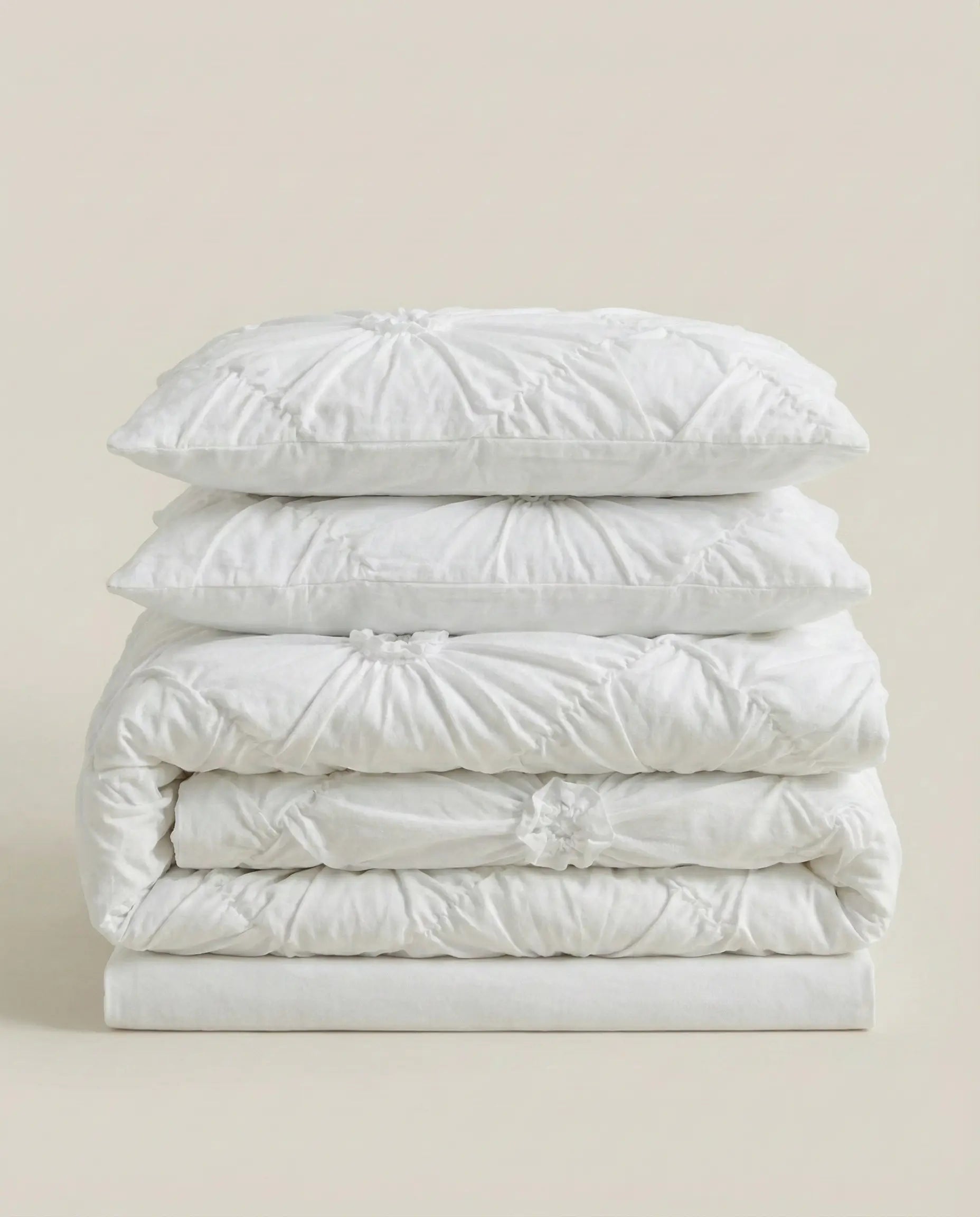 Folded white ruched duvet cover set with matching pillowcases stacked on neutral studio background