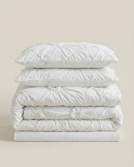 Folded white ruched duvet cover set with matching pillowcases stacked on neutral studio background