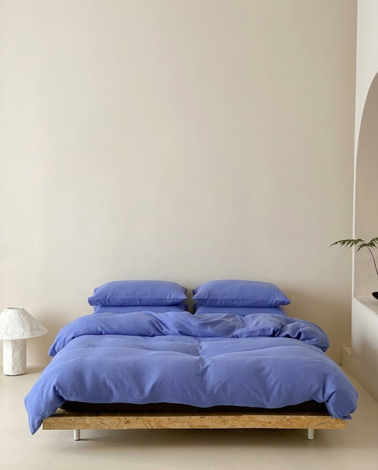 Ultramarine muslin bedding set on a low wooden bed in a minimal bedroom