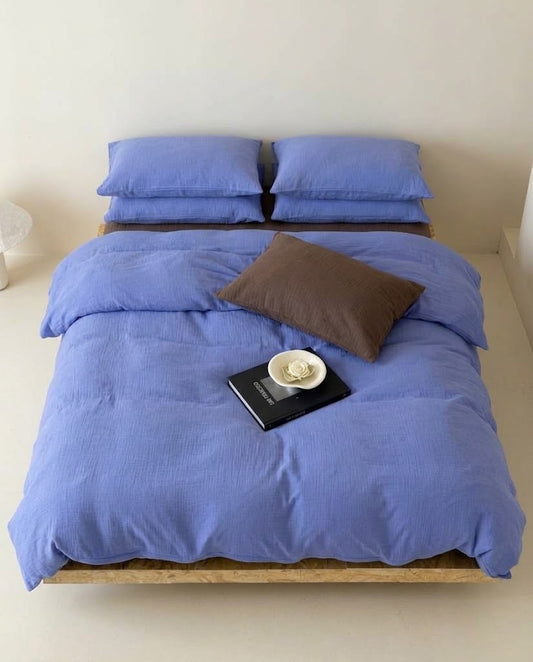 Overhead view of Ultramarine muslin duvet cover set with four pillowcases and a brown pillow