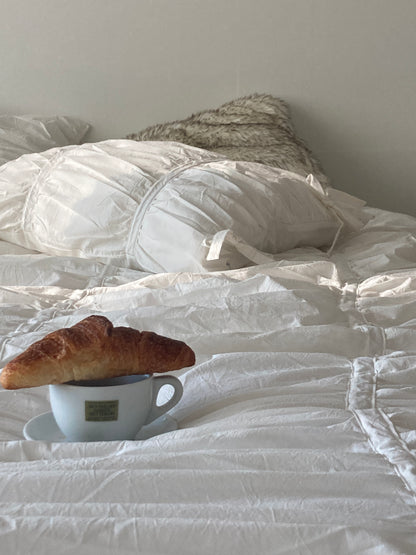 Croissant resting on a coffee cup placed on white ruched bed sheets — cozy breakfast in bed morning scene