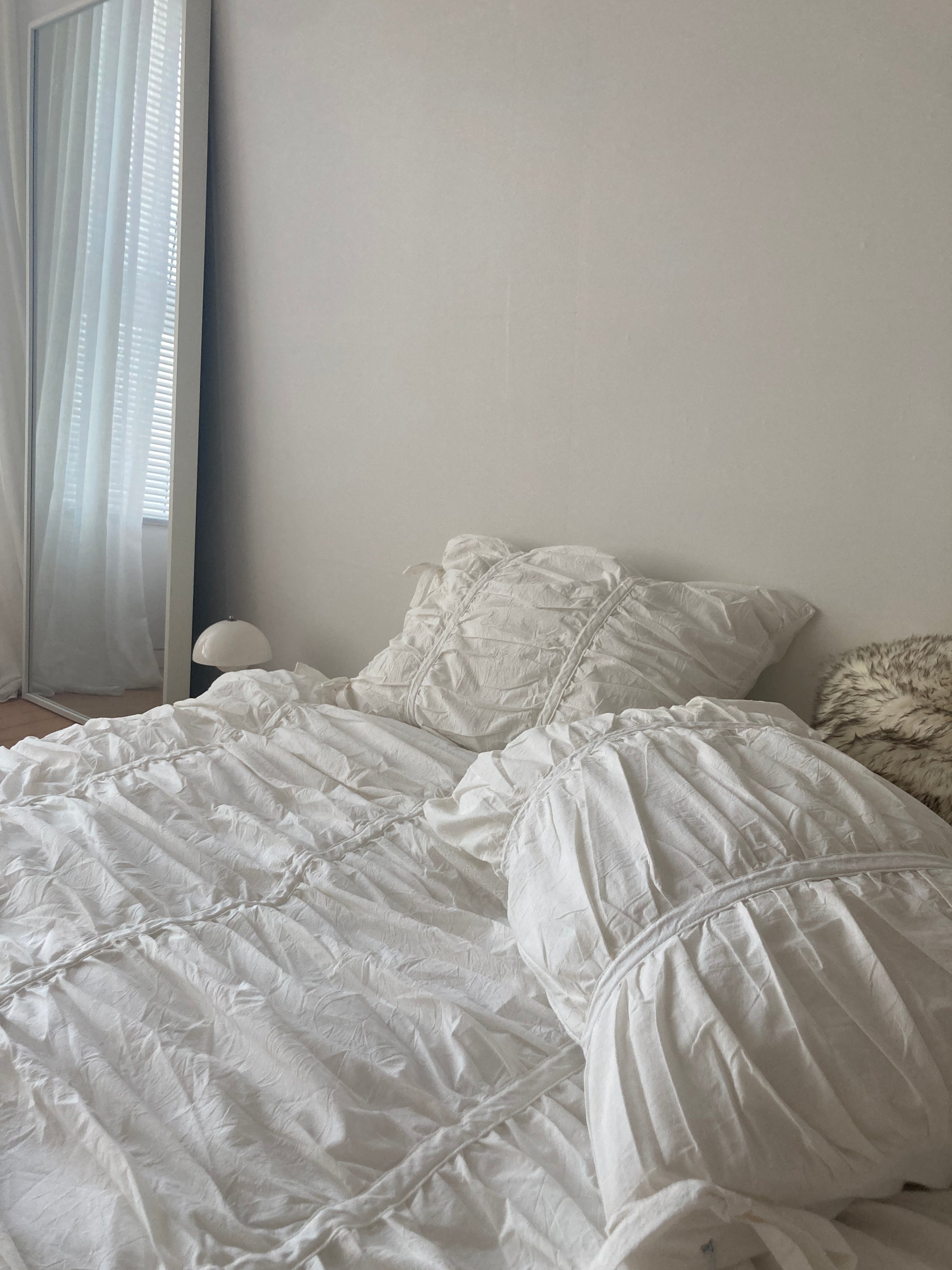 White ruched duvet cover styled on a floor-level bed with soft morning window light and a full-length mirror