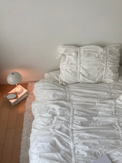 Close-up of a white ruched pillow sham showing gathered cotton texture, next to a glowing Verner Panton bedside lamp